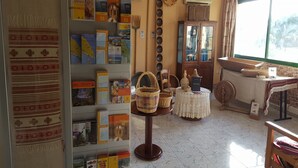 A room with a bookshelf, wicker baskets, a spinning wheel, and a window with curtains. - Mandalena Hotel Apts (Paralimni)