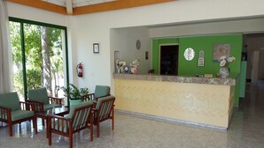 A reception area with a green wall, a reception desk, and a seating area with wooden chairs and a table. - Mandalena Hotel Apts (Paralimni)