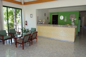 A reception area with a green wall, a reception desk, and a seating area with wooden chairs and a table. - Mandalena Hotel Apts (Paralimni)