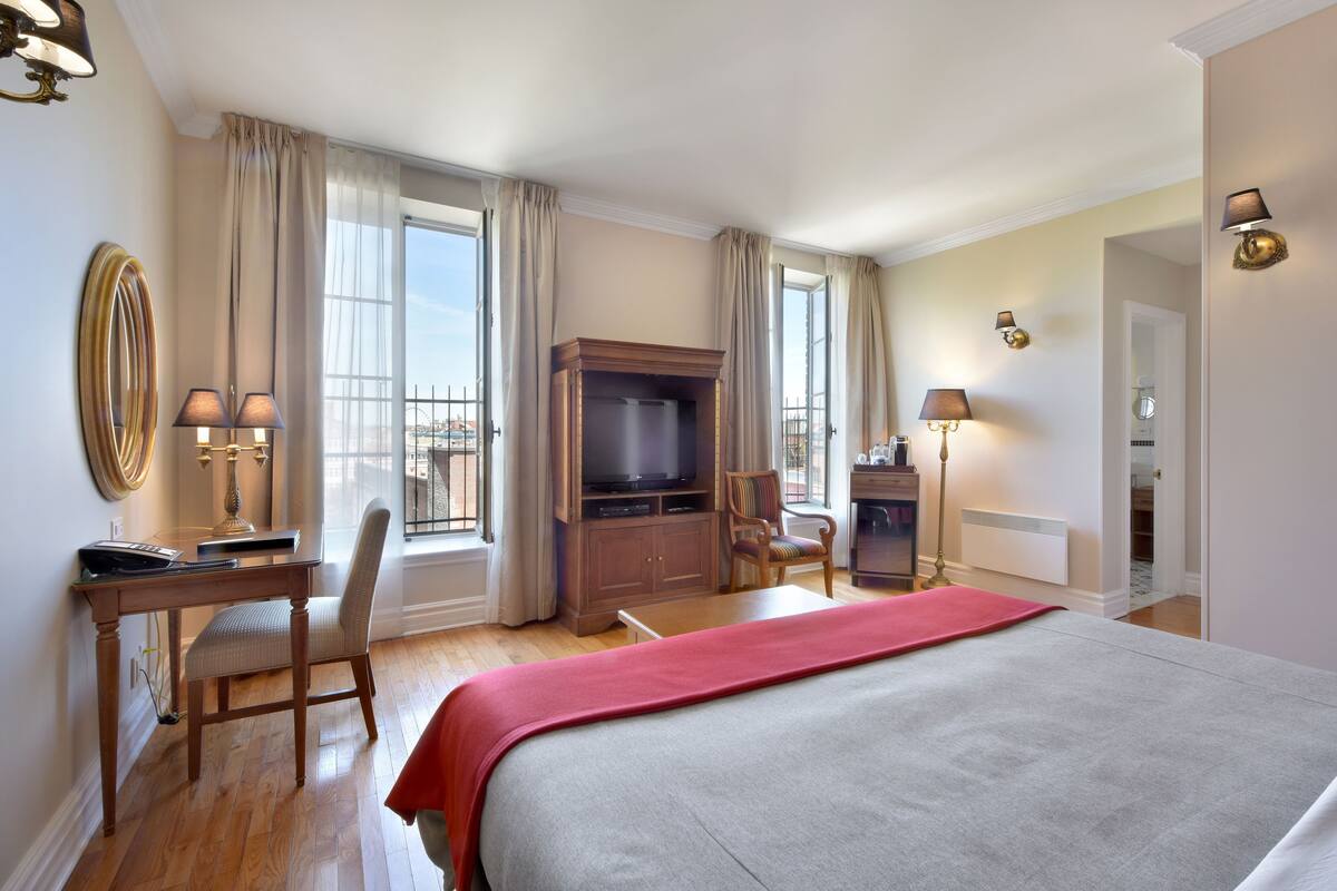 A hotel room with a bed, a desk with a computer, a television, a chair, and a window with curtains.