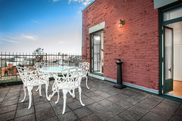 Une terrasse sur le toit avec une table ronde et des chaises blanches, un mur en briques rouges et une vue sur le paysage urbain.