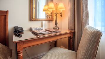 Una habitación de hotel con un escritorio de madera, un teléfono, una lámpara y una silla.