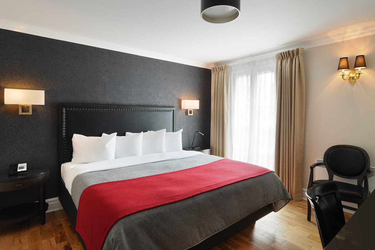 A hotel room with a large bed, two bedside lamps, a desk, and a chair.