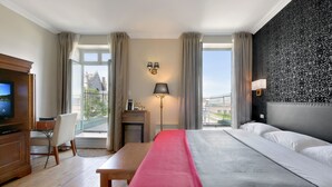 A hotel room with a bed, a desk, a chair, a TV, and a view of a building. - Hotel Bonaparte  (Montreal)