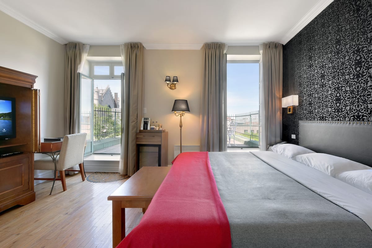 A hotel room with a bed, a desk, a chair, a TV, and a view of a building.