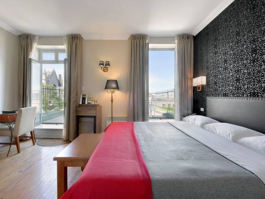 Ein Hotelzimmer mit Bett, Schreibtisch, Stuhl, Fernseher und Blick auf ein Gebäude.