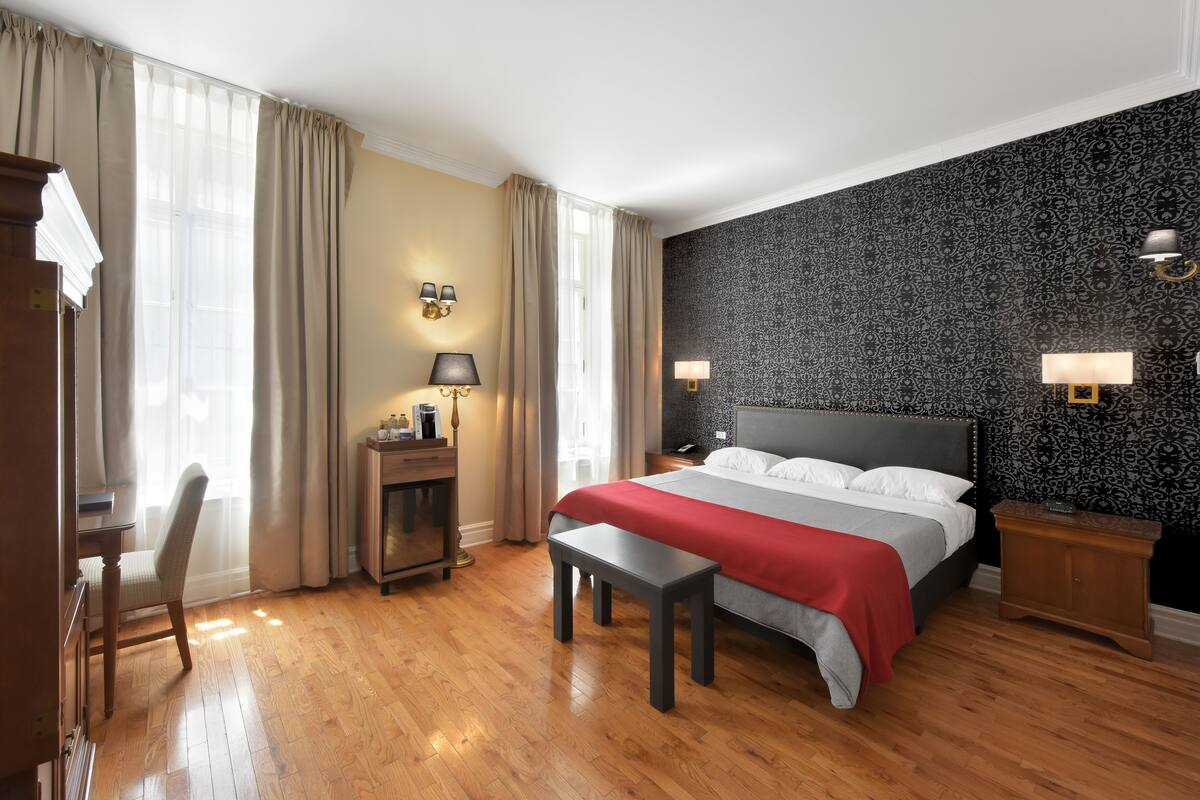 A hotel room with a large bed, a desk, a chair, a bench, and two bedside tables with lamps.