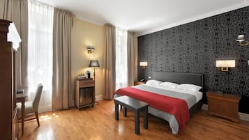 Camera d'albergo con un letto grande, una scrivania, una sedia, una panca e due comodini con lampade.