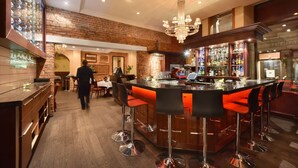 A bar area with a brick wall, a chandelier, and a bar counter with stools. - Hotel Bonaparte  (Montreal)