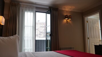Une chambre d’hôtel avec un lit, une fenêtre avec des rideaux, un luminaire fixé au mur et une porte.