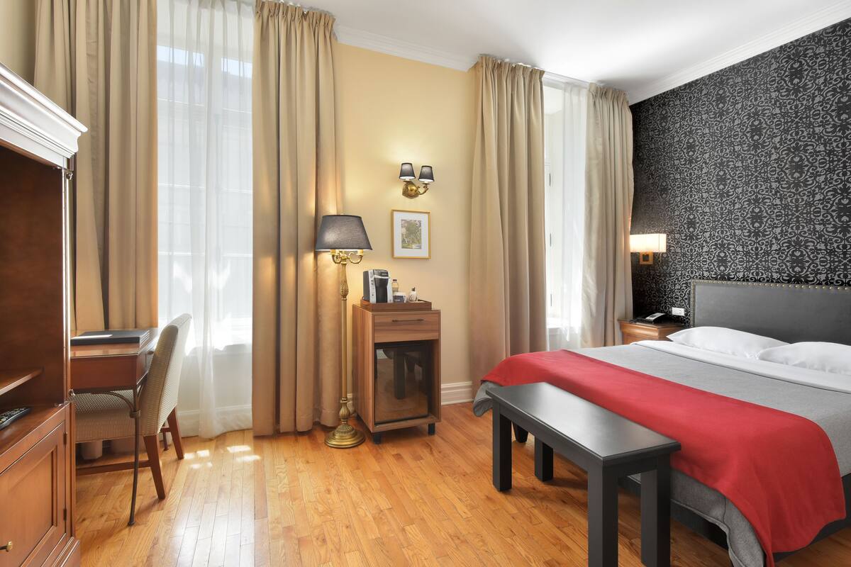 A hotel room with a bed, desk, chair, lamp, and a small table.