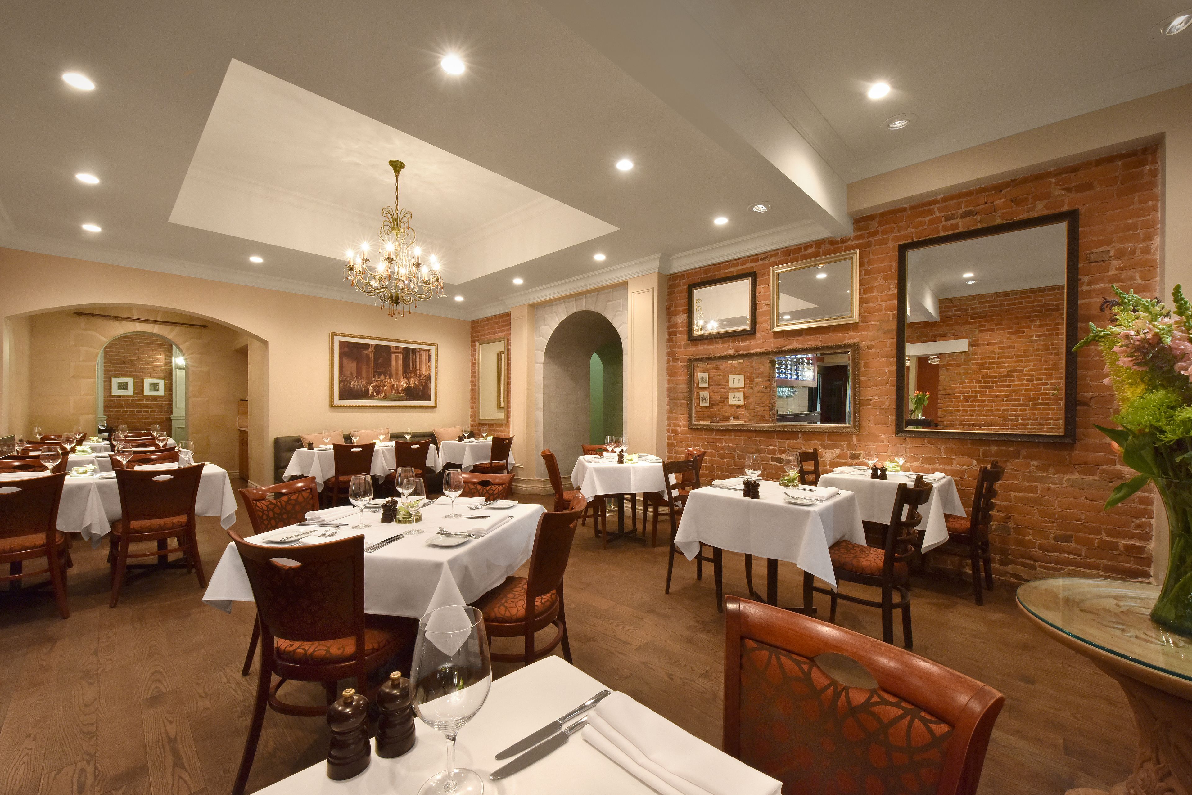 A restaurant with multiple tables and chairs, a chandelier, and brick walls.