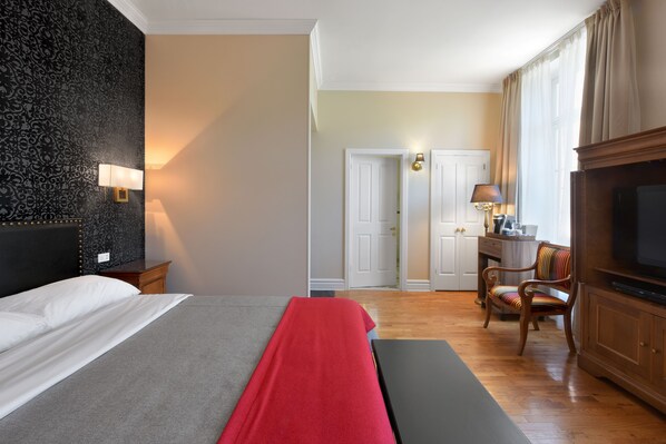 A hotel room with a bed, a desk, a chair, a television, and a lamp.