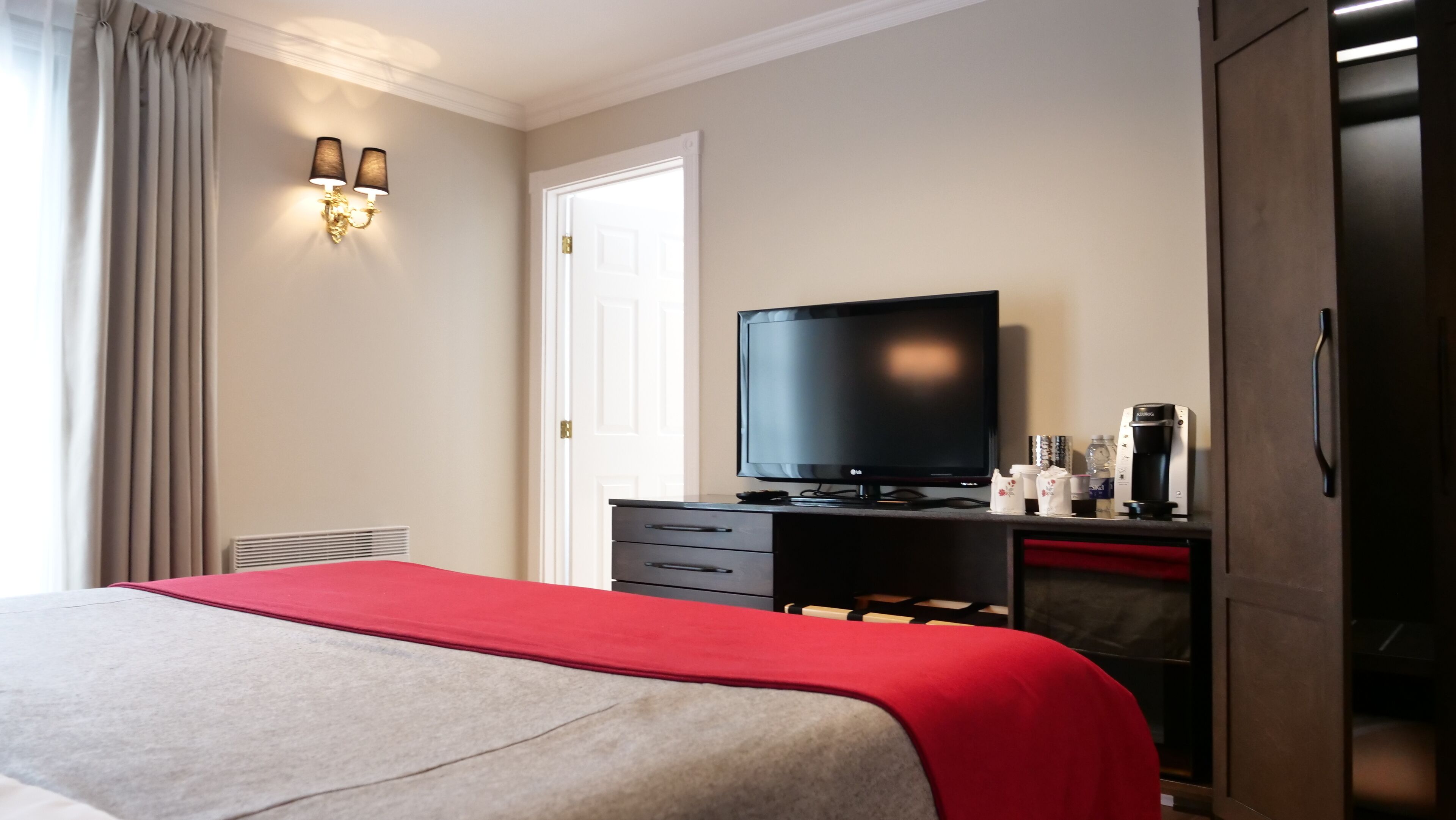 A hotel room with a bed, a television, a coffee machine, and a wardrobe.
