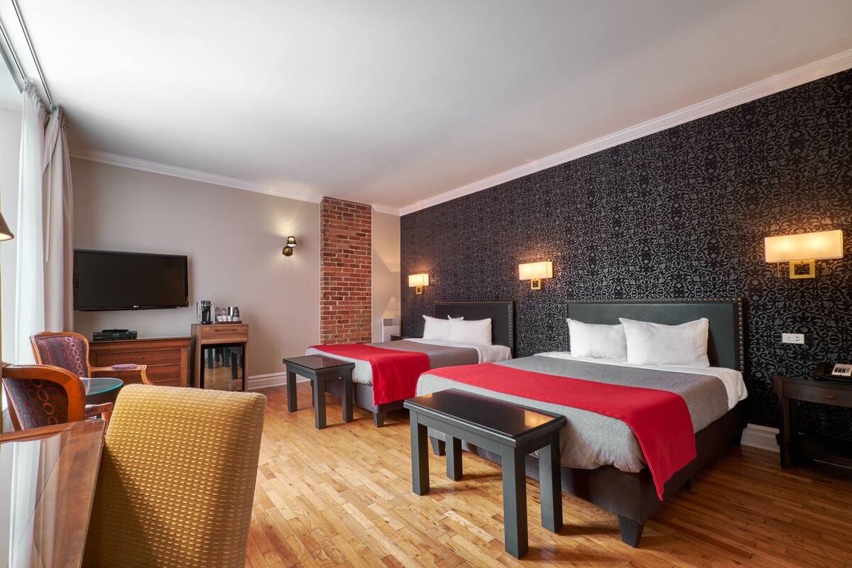 A hotel room with two beds, a TV, a desk, and a chair.