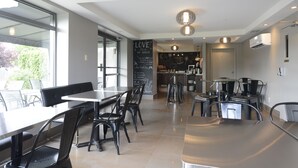 Una cafetería moderna con un amplio ventanal, una pizarra con mensajes inspiradores y diferentes opciones de asientos.