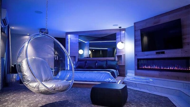 Un dormitorio moderno con una silla colgante, una cama, un televisor y una chimenea.