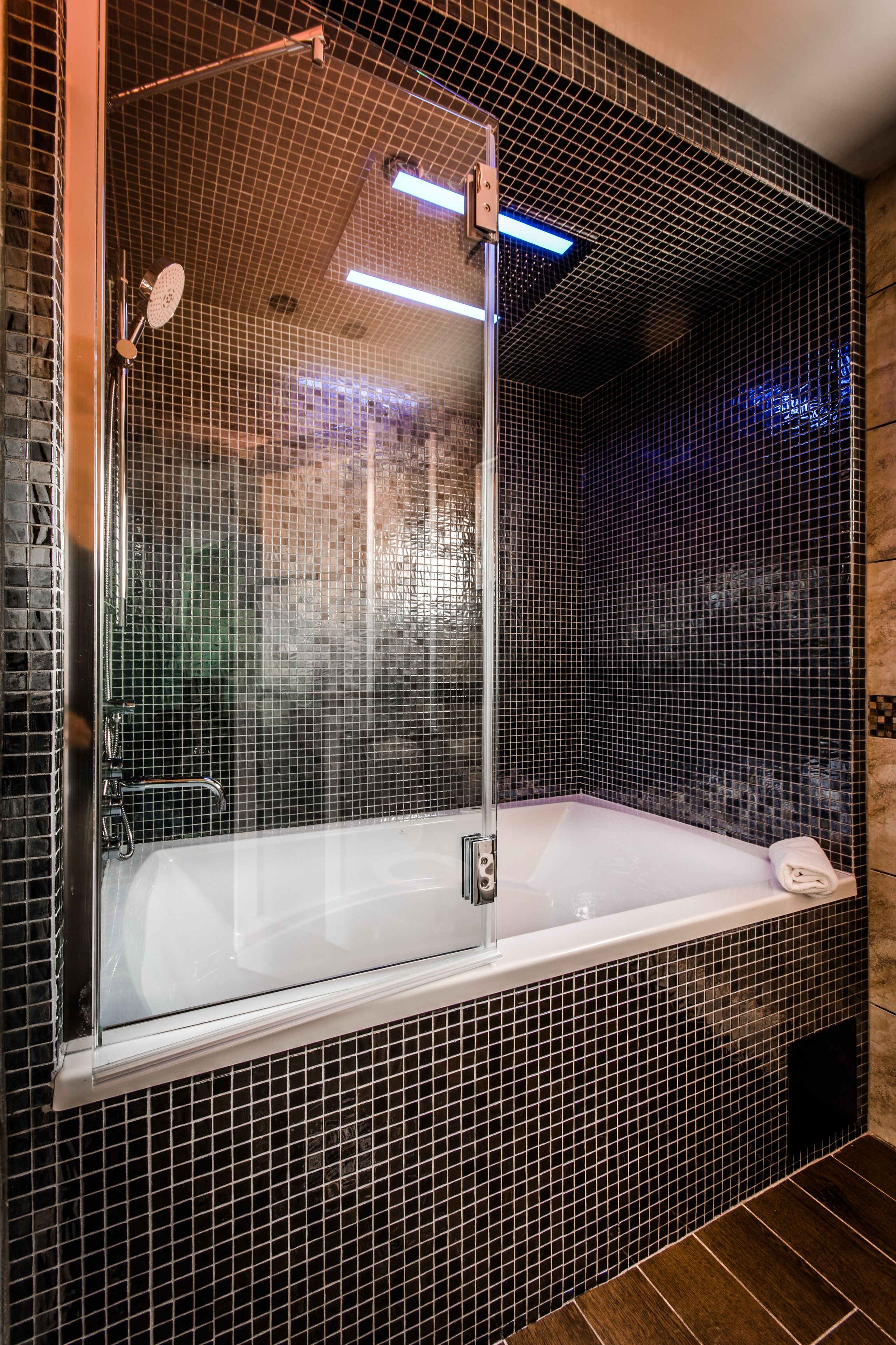 Un baño moderno con una bañera de hidromasaje con mampara de vidrio, una ducha y un perchero para toallas.