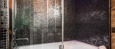 Un baño moderno con una bañera de hidromasaje con mampara de vidrio, una ducha y un perchero para toallas.