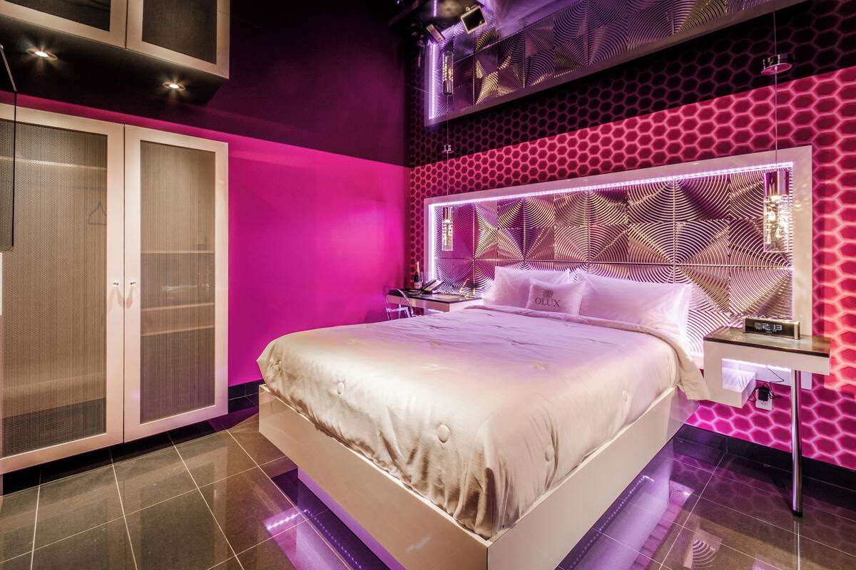 A modern bedroom with a large bed, a walk-in closet, and a unique geometric wall design.