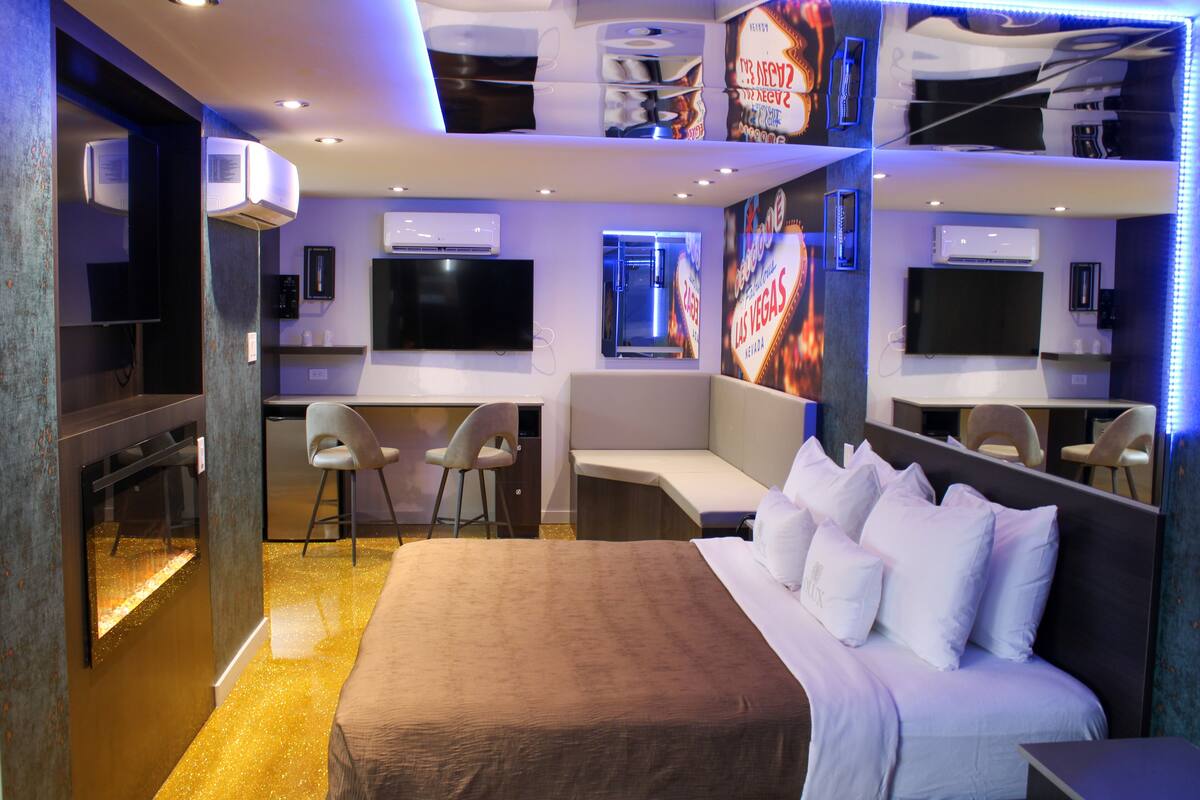 A hotel room with a large bed, a desk, two chairs, and a TV.