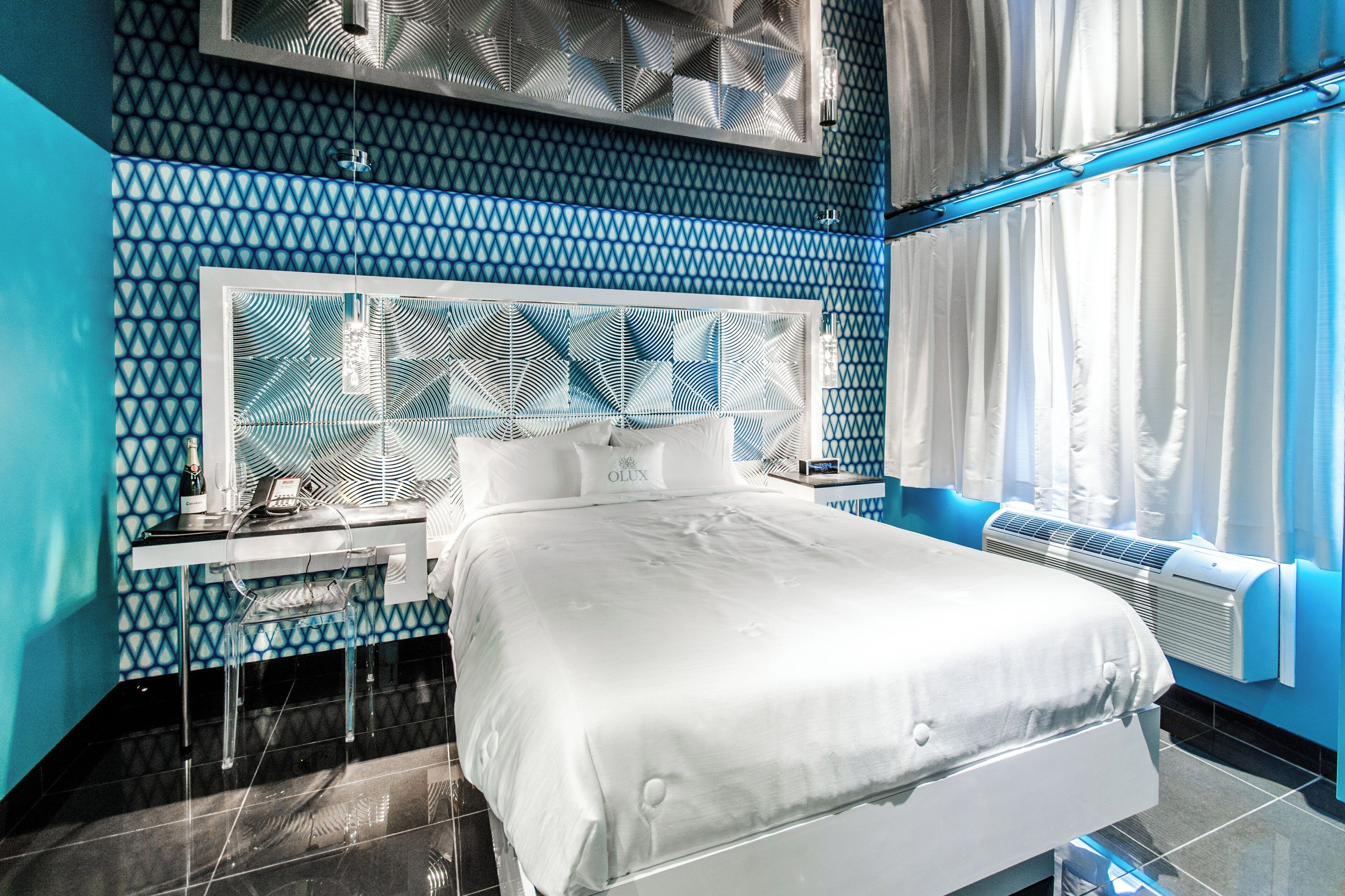 A modern hotel room with a geometric patterned wall, a large bed with white linens, a bedside table with a phone, and a window with curtains.
