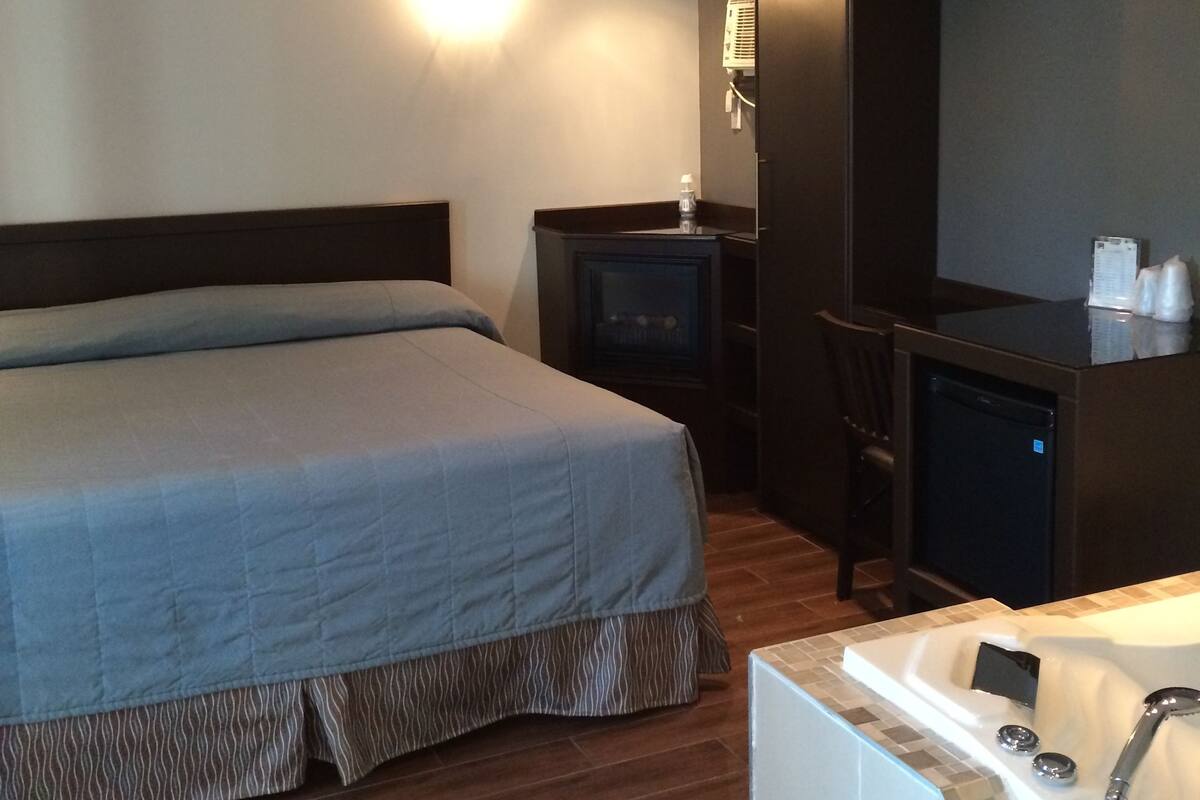 A hotel room with a bed, a small desk with a computer, a chair, and a bathroom with a bathtub and sink.