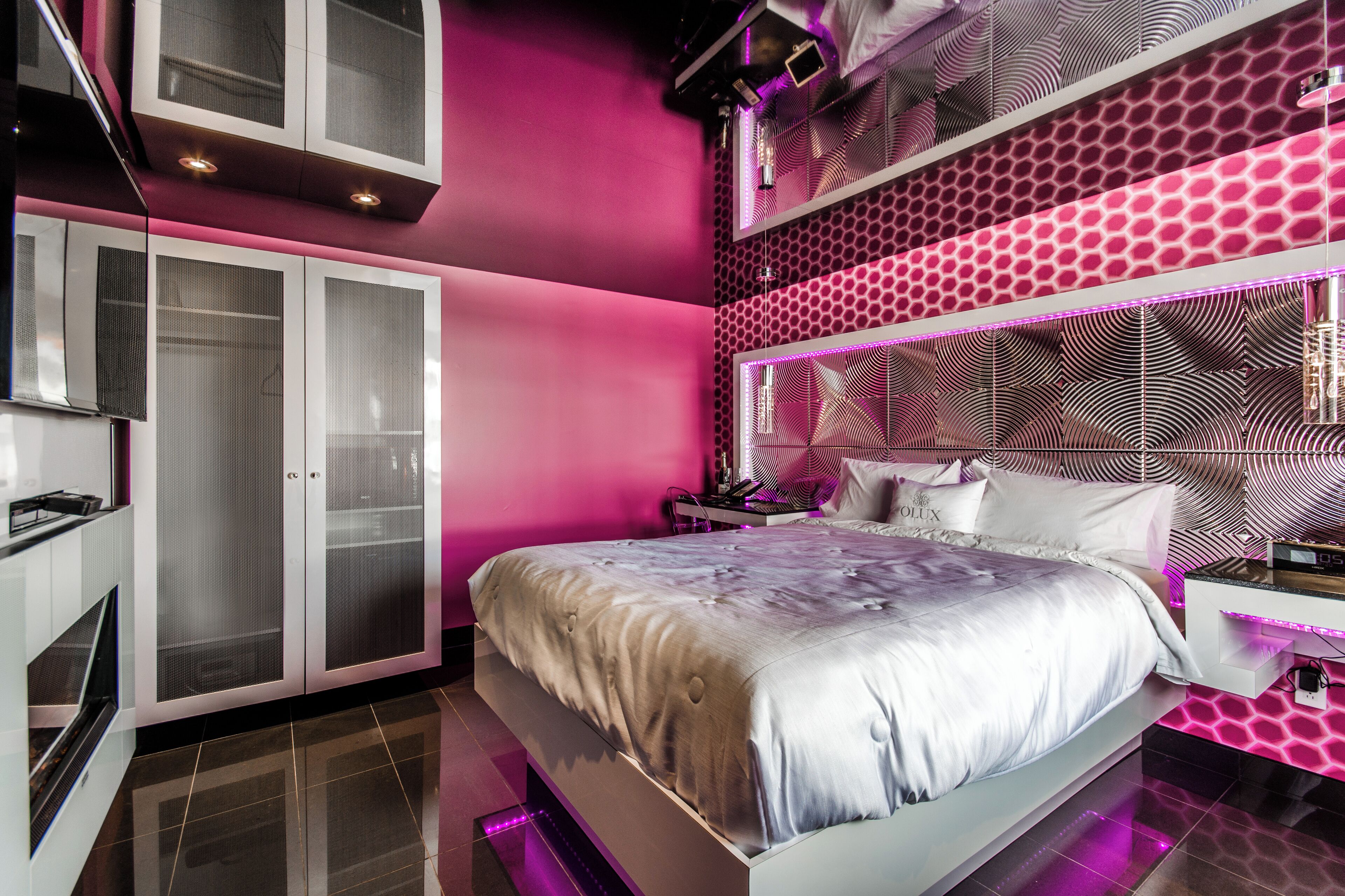 A modern bedroom with a large bed, a wardrobe with glass doors, and a unique patterned headboard.