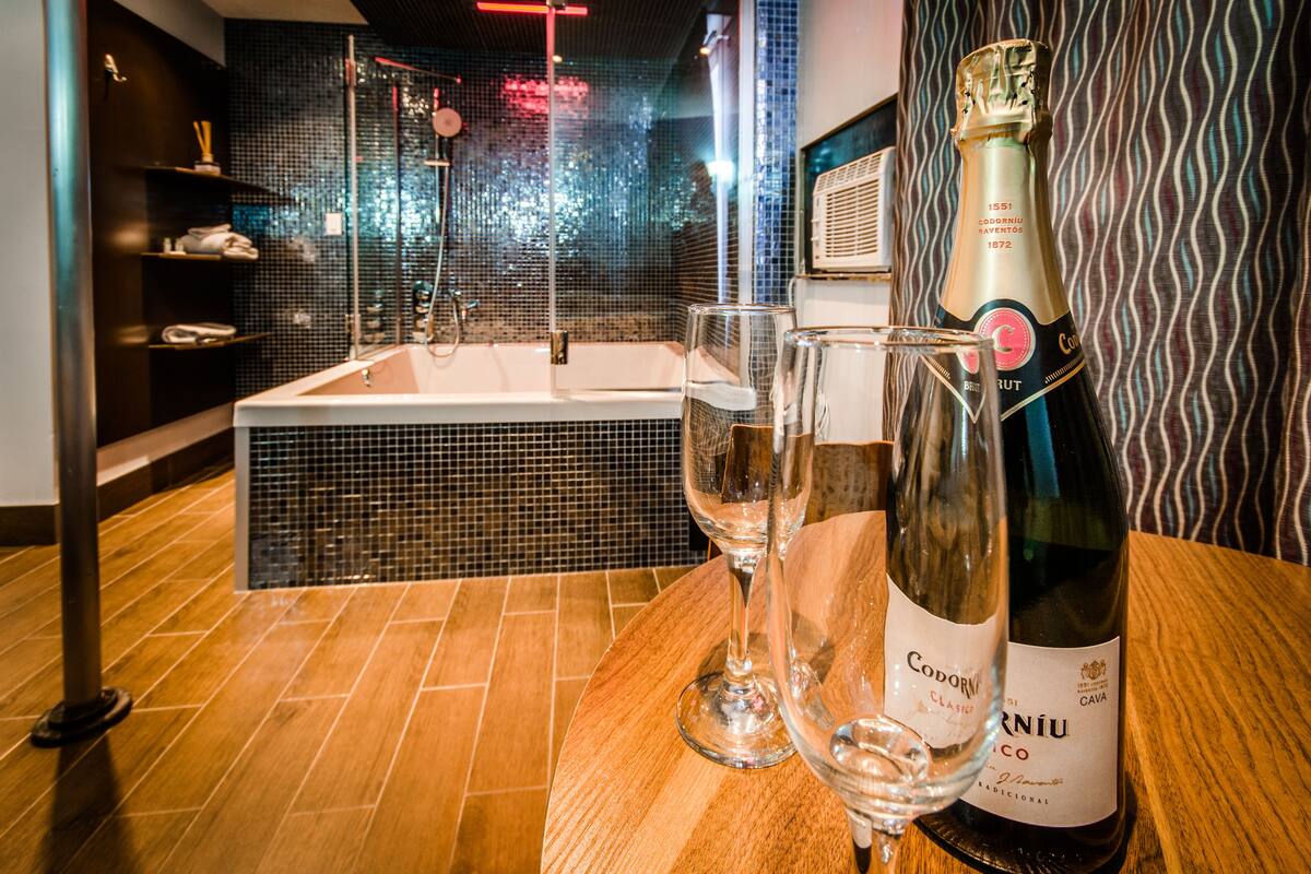 A bathroom with a bathtub, a shower, and a wooden vanity table with a bottle of champagne and two glasses.