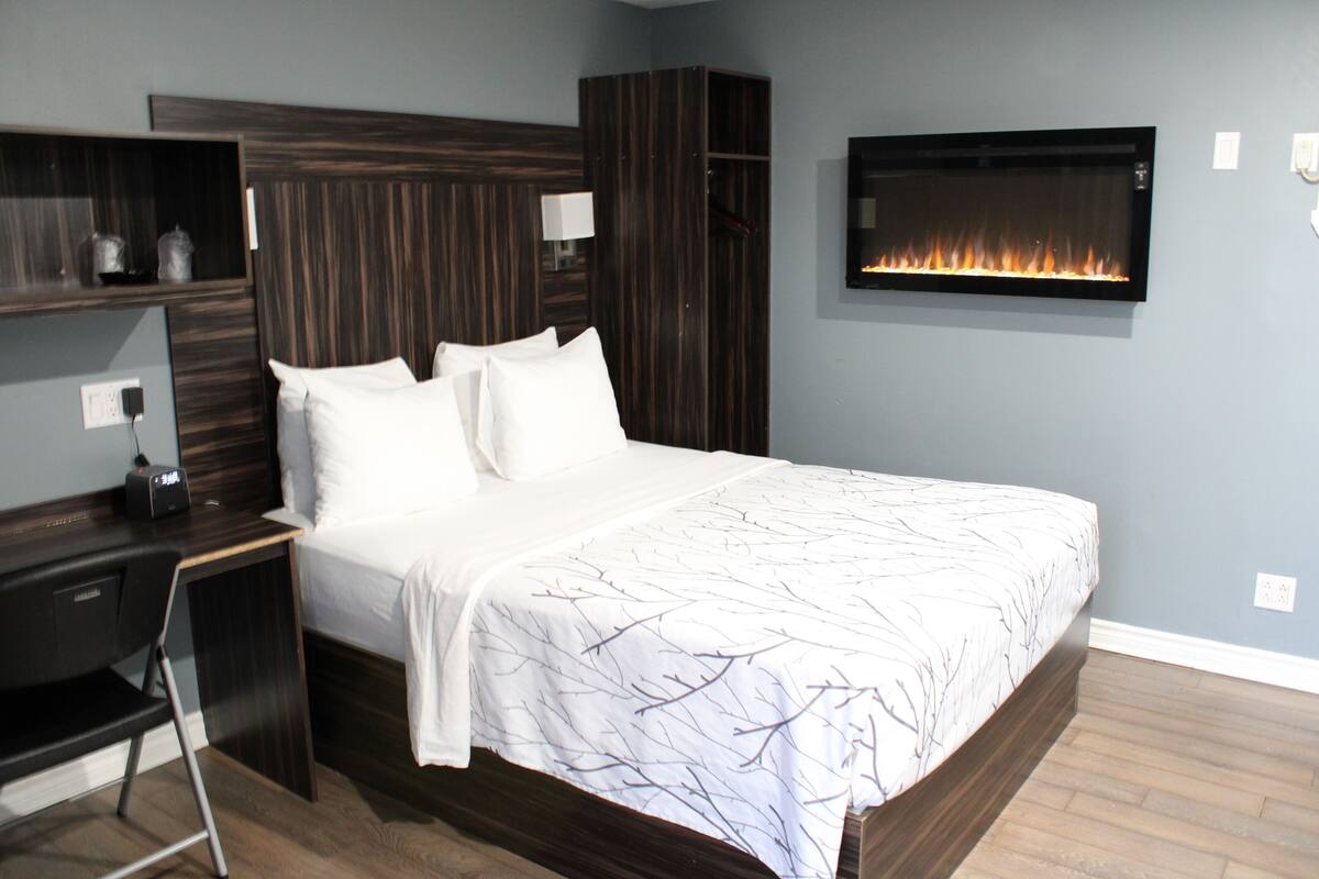 A bedroom with a bed, a desk, a wardrobe, and a wall-mounted fireplace.