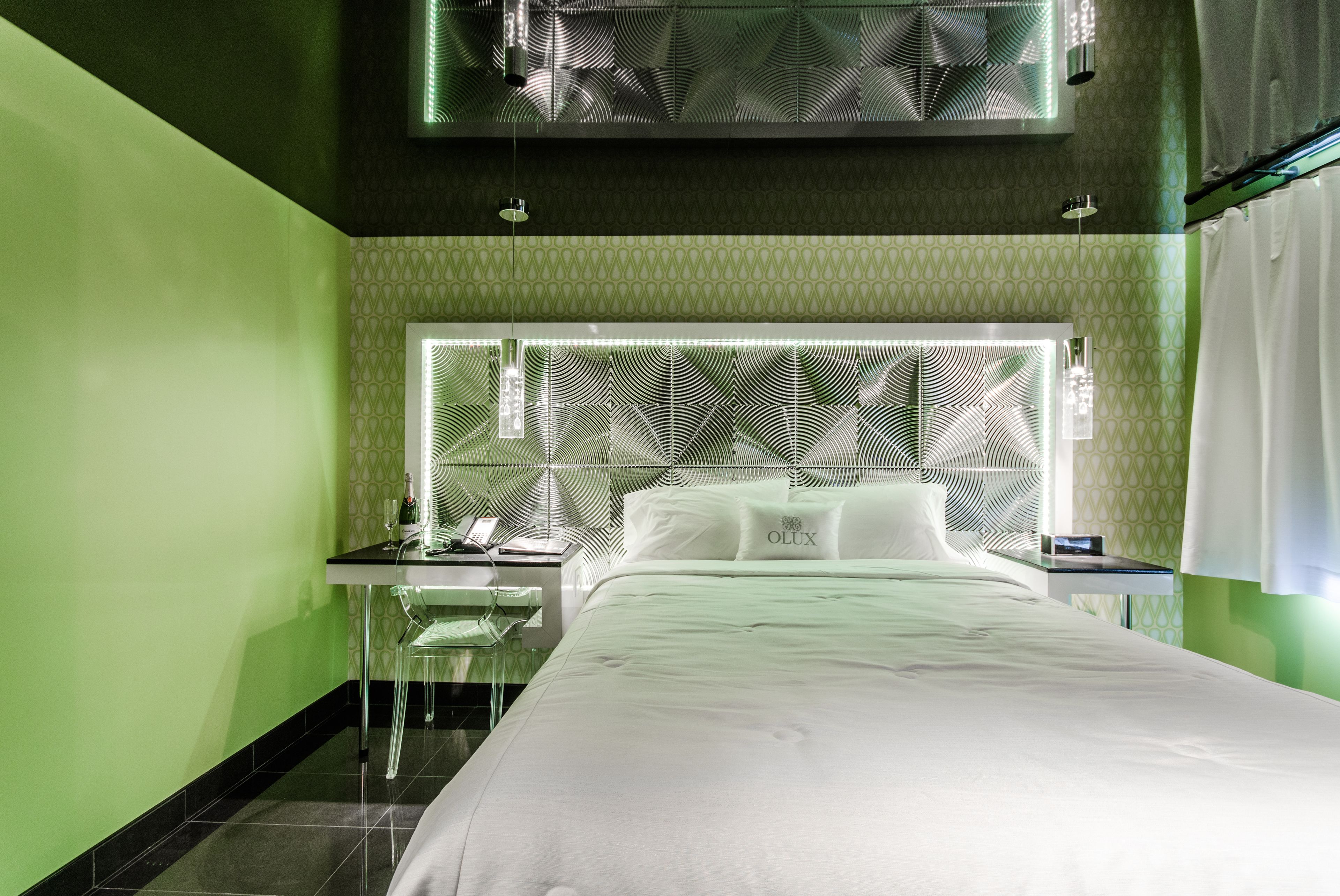 A modern hotel room with a large bed, a desk with a chair, and a patterned headboard.
