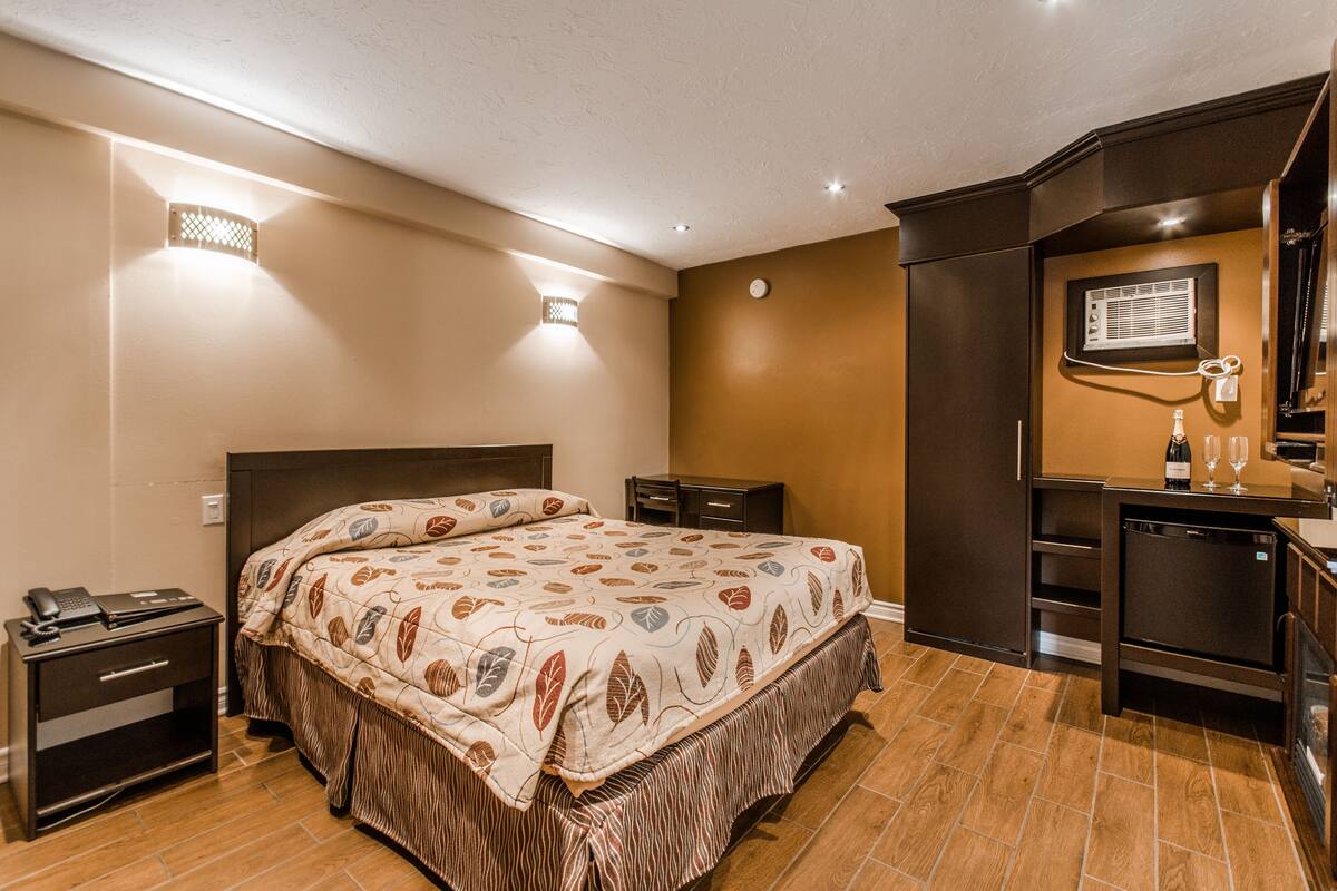 A hotel room with a bed, a nightstand, a dresser, and a small kitchenette.