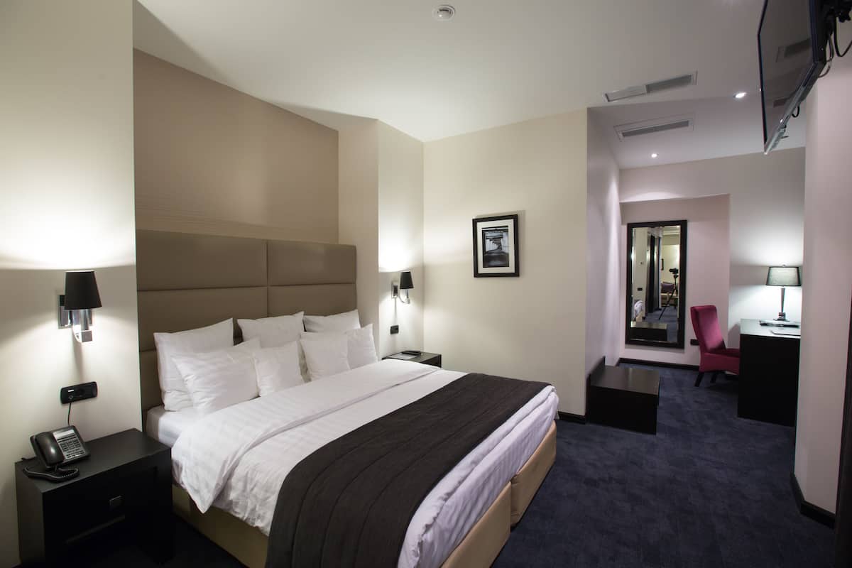 Una habitación de hotel con una cama grande, lámparas de noche, un escritorio con silla y un espejo.