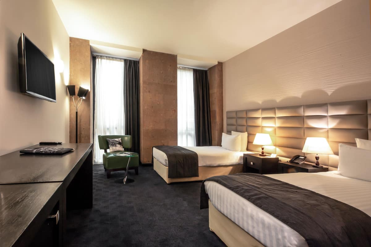 Habitación de hotel con cama, escritorio, silla, televisión y ventana con cortinas.