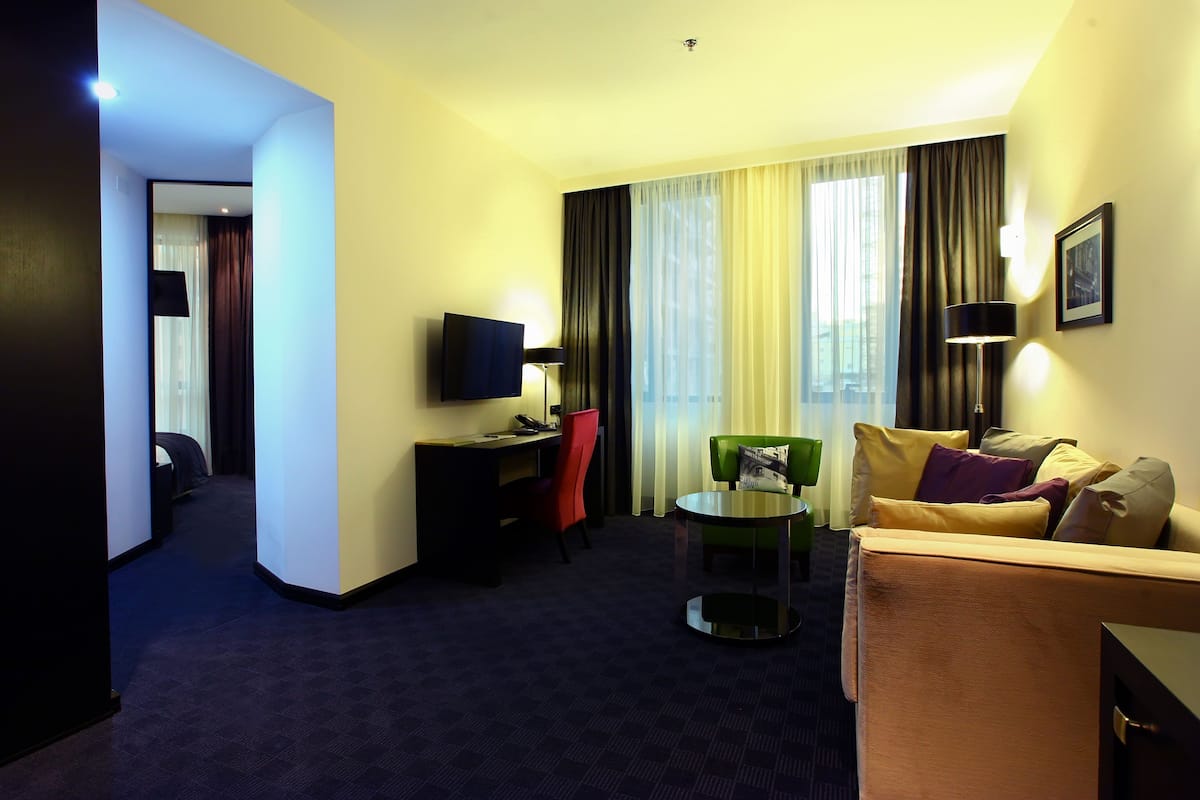 Habitación de hotel con sofá, una mesita, televisor y escritorio con silla.