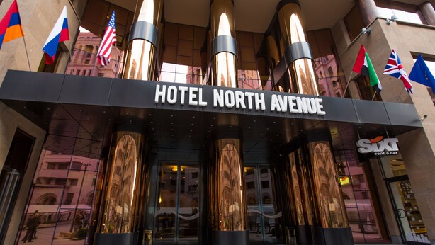 Der Eingang des HOTEL NORTH AVENUE mit großen zylindrischen Säulen und mehreren Flaggen.