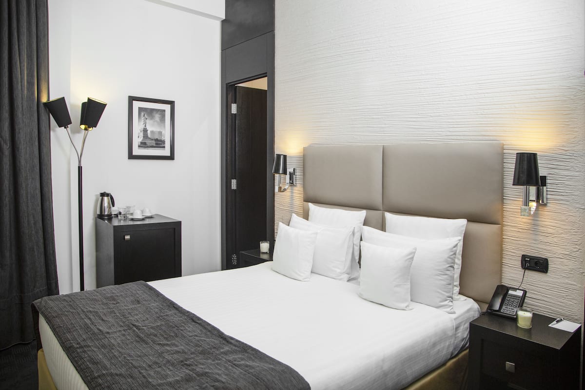 Una habitación de hotel moderna con una cama grande, mesitas de noche, una lámpara, un cuadro enmarcado y una puerta.