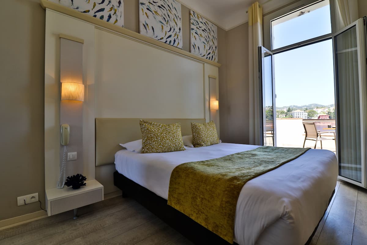 Une chambre d’hôtel avec un grand lit, une table de chevet avec un téléphone et une vue sur l’extérieur grâce à une grande fenêtre.