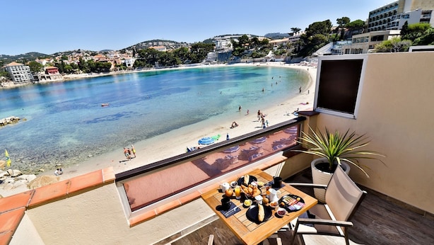 A balcony with a table set for breakfast overlooking a beach. - Golf Hôtel (Bandol)