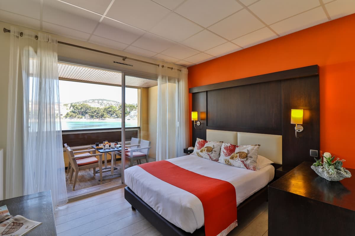 Une chambre d’hôtel équipée d’un lit, d’un bureau, d’une chaise, d’une table et offrant une vue sur l’extérieur.