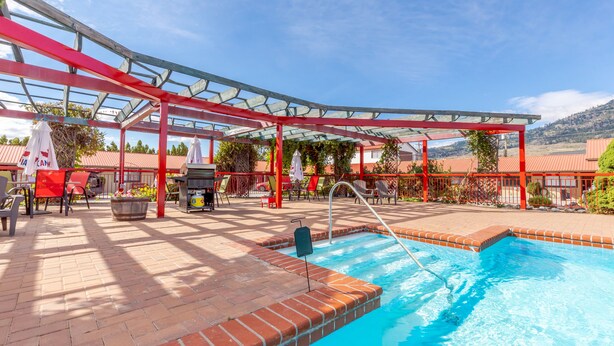 A pool area with a glass roof, red metal framework, and outdoor seating. - Westridge Motor Inn (Osoyoos)