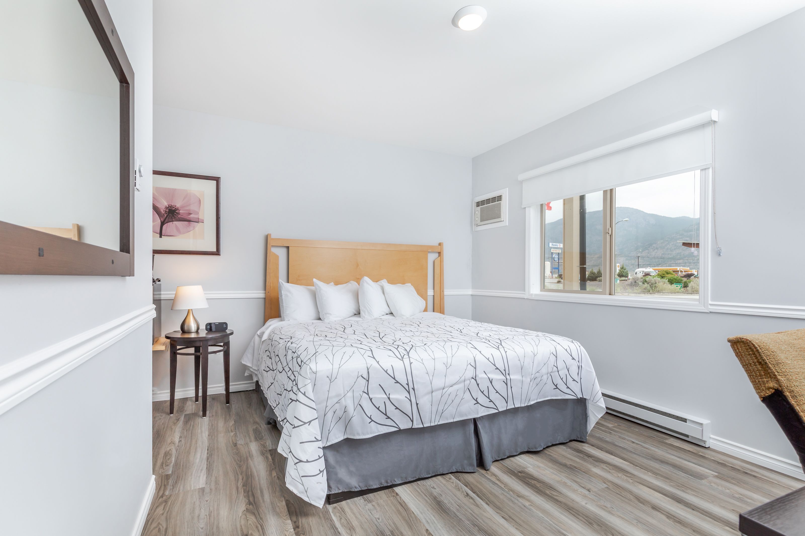 Une chambre à coucher avec un lit, une table de chevet avec une lampe, une fenêtre donnant sur un beau paysage et un tableau encadré au mur.