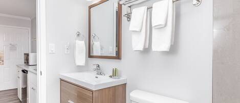A modern bathroom with a white sink, wooden vanity, a toilet, and a towel rack with multiple towels.