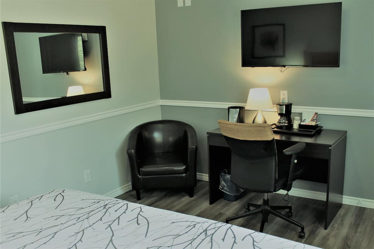 A hotel room with a bed, a desk with a chair, a TV mounted on the wall, and a lamp on the desk.