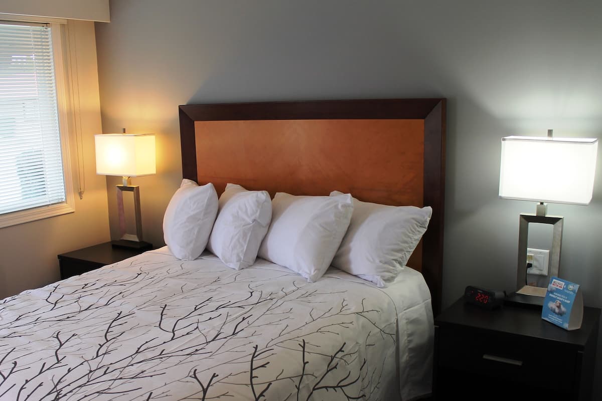 A neatly made bed with a white bedspread featuring a branch pattern, flanked by two bedside tables with lamps, one of which has a digital clock.