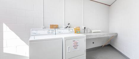 Uma área de lavanderia com máquina de lavar e secadora, bancada com pia e aviso para limpar o filtro da secadora antes e depois de cada uso.