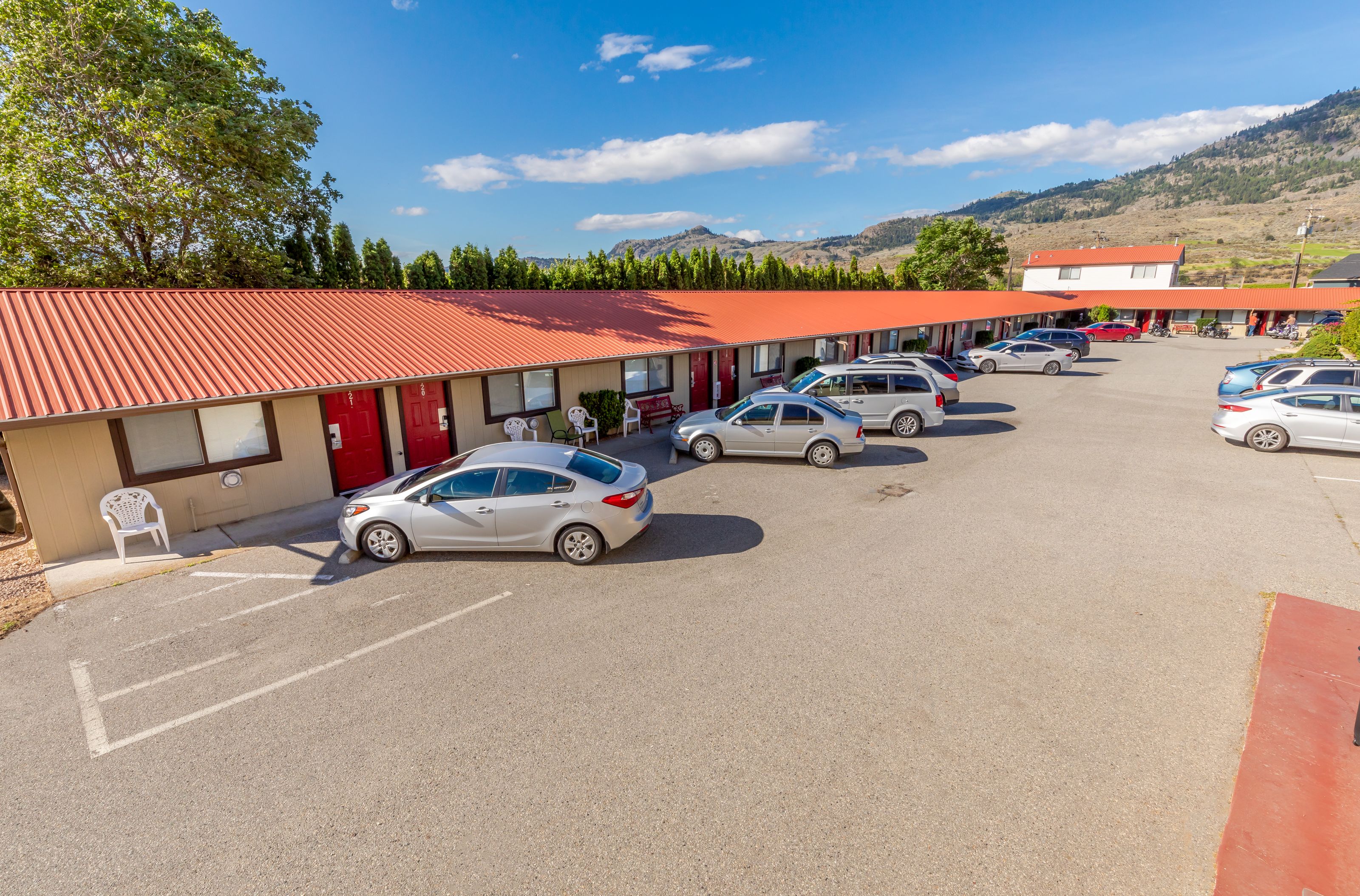 A motel with a red roof, several cars parked in the lot, and a mountainous backdrop.