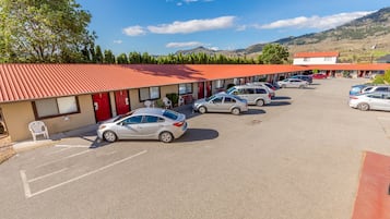 A motel with a red roof, several cars parked in the lot, and a mountainous backdrop.