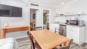 A modern kitchen with white cabinets, a microwave, and a coffee maker. There is a wooden dining table and chairs, and a TV mounted on the wall. - Westridge Motor Inn (Osoyoos)