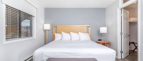 Une chambre d’hôtel bien aménagée, avec un grand lit, des lampes de chevet, un banc et une fenêtre avec des stores.